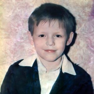 Portrait of young Ukrainian orphan boy Vitaly in a black jacket and white shirt, smiling softly.
